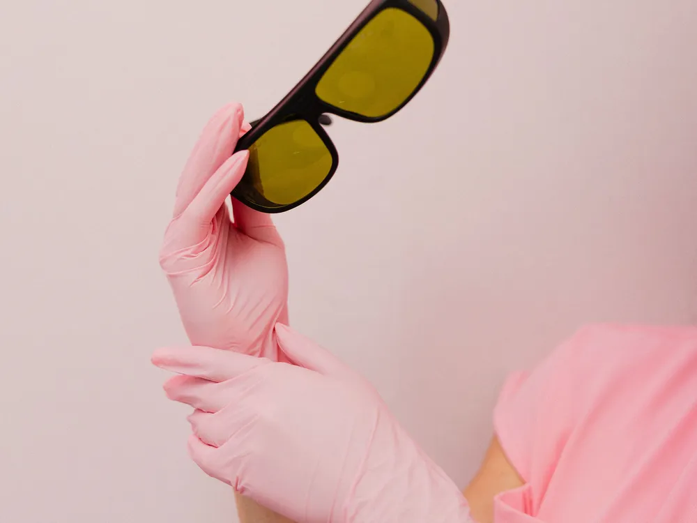 Pink-gloved hands holding a pair of laser goggles