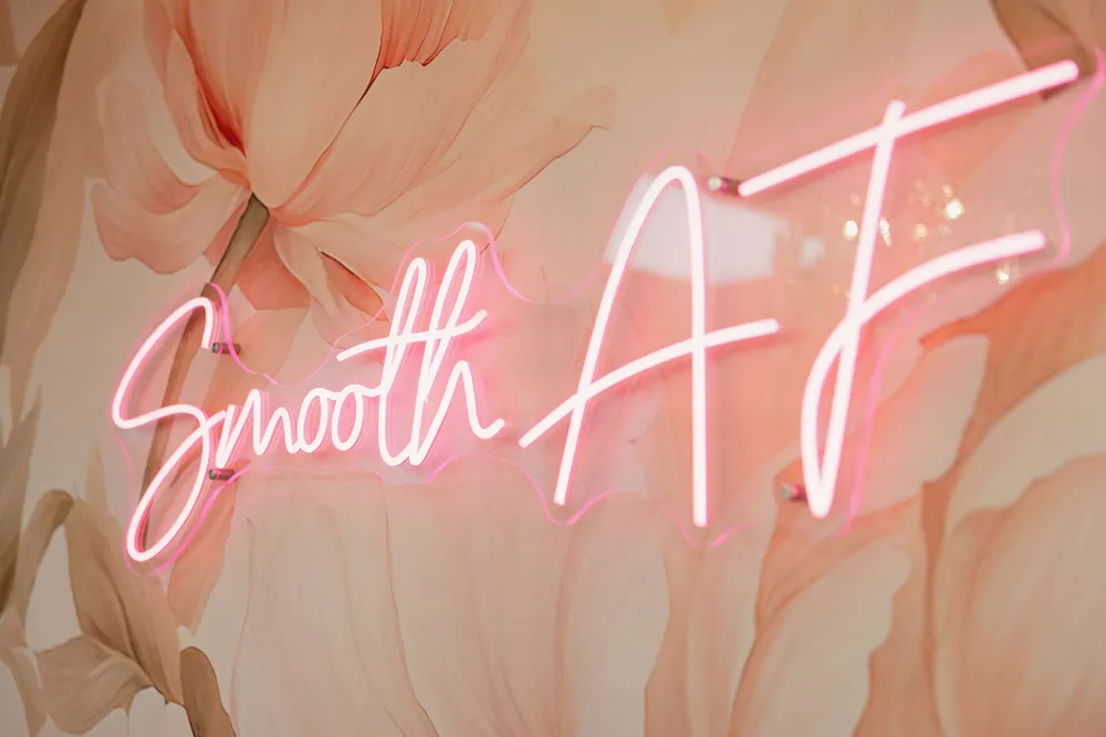 The Smooth AF neon sign glowing over the peony mural at Pink Diamond Laser