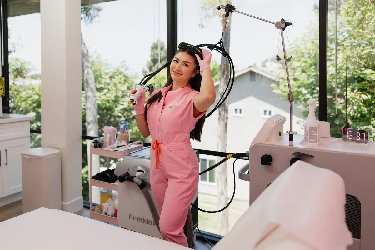 Leslie in pink scrubs in the daylit treatment room at Pink Diamond Laser, lifting the laser handpiece beside the Candela GentleMax Pro