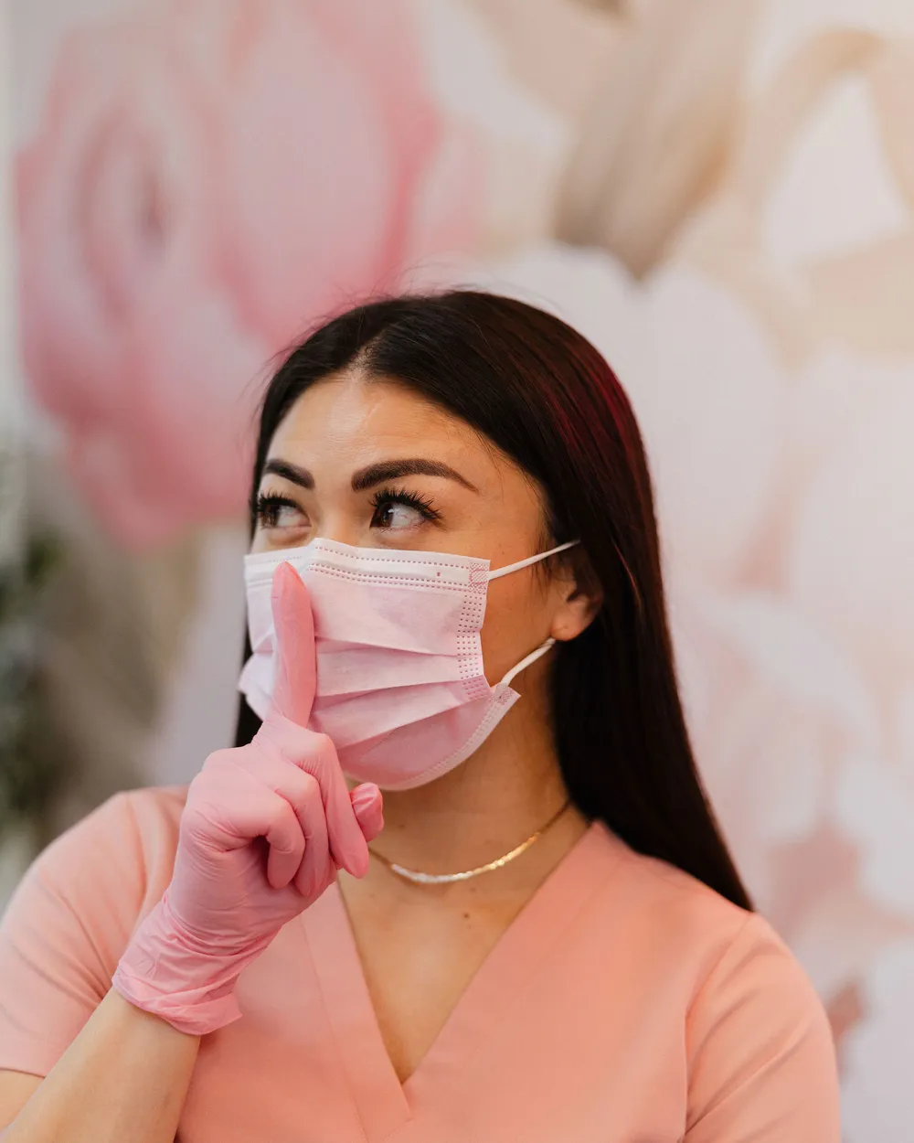 Leslie in a pink surgical mask and gloves, holding a finger to her lips