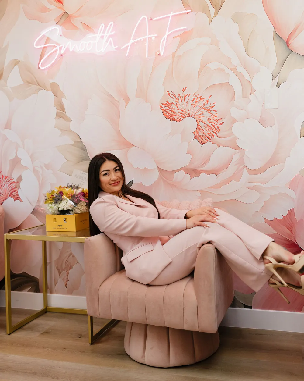 Leslie Nguyen lounging in the blush velvet chair beneath the Smooth AF neon sign in the Pink Diamond Laser lobby